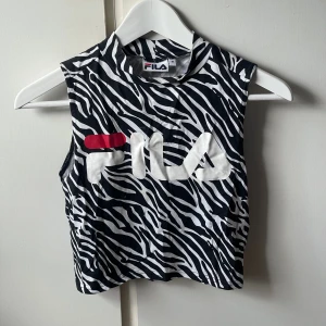 Zebramönstrad ärmlös topp från FILA - Säljer en cool topp från FILA med svartvitt zebramönster och stor logga framtill. Toppen har hög hals och är croppad i modellen, men den är insydd så den motsvarar mer en XS nu! Är alltså inte storlek M längre☺️