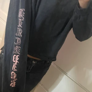 Svart croppad BLACKPINK sweatshirt - Svart croppad sweatshirt från BLACKPINK med rosa tryck på bröstet och längs ena ärmen. Tröjan har rund hals, långa ärmar och relaxed fit. Perfekt för dig som gillar K-pop och vill ha en snygg streetstyle-look.