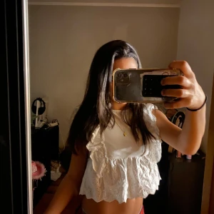 Vit blus med volanger från C - Supersöt vit blus med volanger och broderade detaljer. Croppad modell med ärmlös design och romantisk känsla. Perfekt för dig som gillar en feminin och trendig stil. Luftigt bomullstyg som är skönt mot huden.