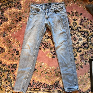 Replay Anbass ljusblå jeans, 31/32 - Säljer ett par Replay Anbass jeans i ljusblå tvätt med klassisk femficksdesign och smal passform. Jeansen har snygga slitningar och detaljer vid fickorna, samt knapp och dragkedja i gylfen. Perfekt för dig som gillar en modern och stilren look. (30) midja 39cm längd 99cm 