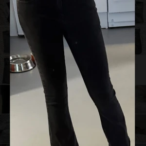 Svarta bootcut jeans från Lindex - Säljer ett par svarta jeans från Lindex med bootcut passform och hög midja. Jeansen har klassiska fem fickor, knapp och dragkedja framtill samt bälteshällor. Materialet är stretchigt denim som sitter snyggt och bekvämt. Perfekt för dig som gillar en tidlös look.