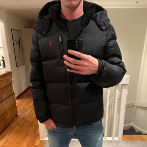 Svart vinterjacka från Polo Ralph Lauren - Säljer en svart vinterjacka från Polo Ralph Lauren i väldigt fint skick. Jackan har en röd broderad logga på bröstet, fickor med dragkedja och en quiltad design. Perfekt för kalla dagar och riktigt snygg till jeans. Storlek L, jackan har inga defekter. Ny pris 5499kr, mitt pris 2499kr. Hör av dig vid intresse av frågor eller fler bilder. Kan gå ner i pris vid snabb affär!😃