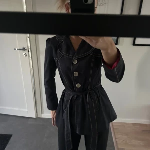 Mörkblå denim kappa/kavaj med bälte från Next - Mörkblå denim kappa/ kavaj från Next med kontrastvita sömmar, stora dekorativa knappar och ett matchande bälte i midjan. Bra skick.