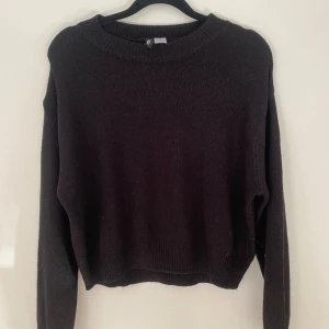 Svart stickad tröja med rund hals - En enkel svart stickad tröja med rundad hals och långa ärmar. Tröjan har ribbade muddar vid ärmslut och nederkant, vilket ger en clean och chill look. Perfekt för lager-på-lager och passar till jeans eller kjol.