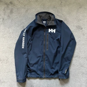 Helly Hansen vindjacka  - Tja, säljer nu en HH vindjacka | Svin snygg och perfekt nu i höst med ett varmare plagg under | Använd och finns lite smuts men inte mycket alls så i väldigt bra skick | Storlek XS-S och passar mig som är 175 | Kom privat för fler bilder eventuellt frågor, mvh Max 🤗