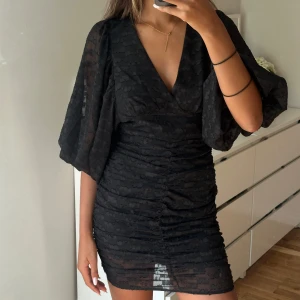 Svart kort klänning med puffärm - Säljer en svart kort klänning med v-ringning och puffiga, transparenta ärmar. Klänningen har ett diskret prickigt mönster och snygg rynkning längs hela framsidan. Perfekt för dig som gillar trendiga detaljer och en feminin siluett. Bilderna är från en annan säljare här på Plick 😙
