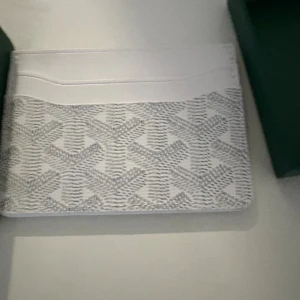 Vit plånbok  - Snygg och stilren vit plånbok  med klassiskt mönster i grått. Plånboken har flera fack för kort och är tillverkad i exklusivt skinn. Perfekt för dig som vill ha något lyxigt och unikt i fickan.