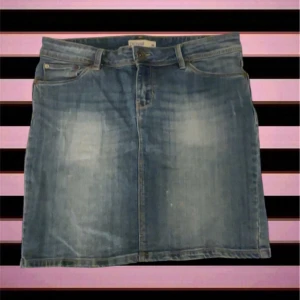 Blå jeanskjol från Lindex - Säljer en klassisk blå jeanskjol från Lindex med fem fickor, bälteshällor och knappstängning fram. Kjolen har en rak passform och är i kort modell, perfekt för dig som gillar enkel och tidlös denimstil.