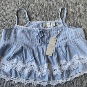 Blå- och vitrandig sovlinne Calypso - Supersöt blå- och vitrandig sovlinne från Calypso i 100% bomull. Toppen har tunna axelband, knytning fram och fina spetsdetaljer i vitt längs nederkant och bröst.  Mått Över bröstet: ca 52 cm Längd från axeln och ner: ca 43-51 cm  100% bomull