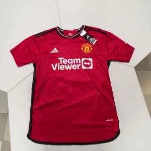Manchester United Rashford 10 tröja - Säljer en officiell Manchester United matchtröja från Adidas med Rashford och nummer 10 på ryggen. Tröjan är röd med svarta detaljer, vit logga och klubbmärke på bröstet. Kortärmad med snyggt mönster i tyget och svart-vit-randig krage. Materialet är lätt polyester.