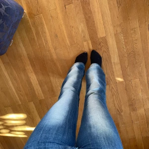 Blå bootcut jeans från Cheap Monday - Säljer ett par blå jeans från Cheap Monday med bootcut-modell. Jeansen har en klassisk femficksdesign, snygga slitningar och en cool patch med Cheap Monday-loggan bak. Materialet är jeans och färgen är mellanblå med ljusare tvättade partier.