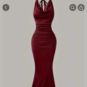 Vinröd långklänning med halterneck - Supersnygg vinröd långklänning med halterneck och draperad urringning. Klänningen har figurnära passform och är tillverkad i ett glansigt, stretchigt material som ger en lyxig känsla. Perfekt för dig som vill sticka ut med en elegant och modern look.