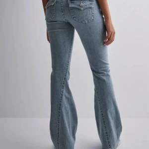 Bootcut ljusblå jeans med fickdetaljer - Snygga ljusblå bootcut jeans med klassiska fickor bak och fram, samt dekorativa sömmar och knappdetaljer på bakfickorna. Jeansen har låg midja och är tillverkade i mjukt denim-material som ger en skön passform och cool siluett.