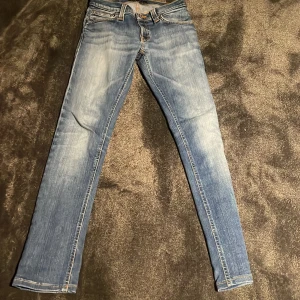 Blå skinny jeans från Nudie Jeans - Snygga ljusblå skinny jeans från Nudie Jeans med klassisk femficksdesign och orangea sömmar. Jeansen har en smal passform, normal midja och är tillverkade i mjukt bomullsmaterial. Bakfickorna har Nudie Jeans signaturbroderi i orange.