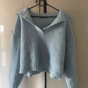 Ljusblå stickad tröja från Gina Tricot - Supermysig ljusblå stickad tröja från Gina Tricot med krage och v-ringning. Tröjan har en loose passform, ribbstickat material och långa ärmar. Perfekt för lager-på-lager och chill dagar.