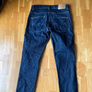 Mörkblå jeans från Nudie Jeans Co - Snygga mörkblå jeans från Nudie Jeans Co med klassisk femficksdesign och kontrastsömmar. Jeansen har rak passform och är tillverkade i robust denim av bomull. Jeansen är oanvända och inköpta för 1600. Model Grim Tim
