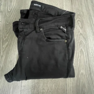 Svarta Replay Hyperflex jeans - Svarta Replay Hyperflex jeans med klassisk femficksdesign och smal passform. Jeansen är tillverkade i stretchigt material för extra komfort och har diskreta Replay-loggor vid fickorna. Perfekta för dig som gillar en stilren och modern look.