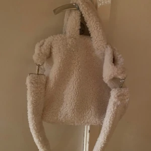 Vit fluffig axelväska i teddy - Supermysig vit axelväska i teddy-material med fluffig yta och rundad form. Väskan har både handtag och en bred axelrem som går att ta av med metallspännen. Insidan har ett fack med dragkedja och gott om plats för dina grejer. Köpt ifrån Lindex för något år sedan men är använd ca en gång.                               Priset är diskuterbart så lägg ett prisförslag om du är intresserad!!