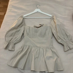 Beige blus med puffärmar och rosett - Supersöt beige blus med puffiga  ärmar, volang nertill. Öppen rygg med stor rosett som knyts. Aldrig använd men ingen prislapp kvar. Helt som ny med inga defekte🩷