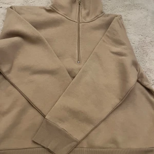 Beige half zip sweatshirt från Kappahl - En stilren beige sweatshirt från Kappahl med half zip-dragkedja och hög krage. Tröjan har långa ärmar, ribbade muddar och är tillverkad i mjuk bomullsmix. Perfekt för lager-på-lager och chill dagar.
