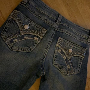 Blå jeans med broderade fickor Gina Tricot - Snygga blå jeans från Gina Tricot i storlek 158. Jeansen har broderade bakfickor med dekorativa sömmar och silvriga knappar. Klassisk femficksmodell med dragkedja och knapp framtill. Perfekt för dig som gillar detaljer och en cool look.