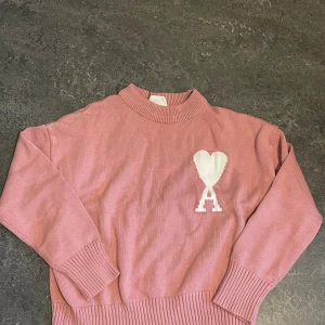 Rosa stickad tröja från Ami Paris - Säljer en rosa stickad tröja från Ami Paris med deras ikoniska vita hjärta och A på bröstet. Tröjan har ribbade muddar, hög hals och är långärmad. Perfekt för dig som vill ha en snygg och trendig look med en touch av streetstyle. (oanvänd) passar också för S 