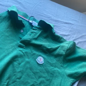 Grön pikétröja från Moncler - Snygg grön pikétröja från Moncler med klassisk krage och knappar framtill. Tröjan har Moncler-logga på bröstet och är tillverkad i bomull, perfekt för en clean och sportig look.