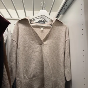 Beige stickad tröja med krage H&M - Beige stickad tröja från H&M med v-ringning och bred krage. Tröjan har trekvartsärm och ribbade detaljer vid ärmslut och nederkant. Perfekt för lager-på-lager och chill stil.