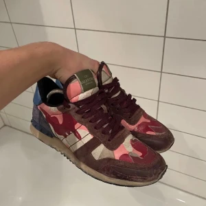 Valentino Rockrunner - Säljer ett par Valentino Rockrunner sneakers med snyggt kamouflagemönster i vinrött, rosa, beige och blått. Skorna har rund tå, platt sula och snörning. Materialmix av mocka och textil, med coola detaljer och logga på tungan.