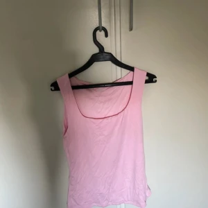Ljusrosa ärmlös linnetopp - Säljer en ljusrosa linnetopp med breda axelband och rundad halsringning. Toppen är enkel och stilren, perfekt för dig som gillar en clean look. Materialet känns mjukt och lätt, och modellen är normal i passningen. Passar dig som vill ha en basic topp i garderoben. Aldrig använt