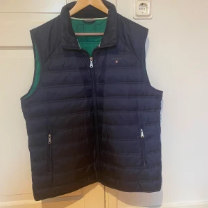 Mörkblå dunväst från GANT - Snygg mörkblå dunväst från GANT i storlek 2XL. Västen är liten i storlek och passar därför bättre på en XL. 