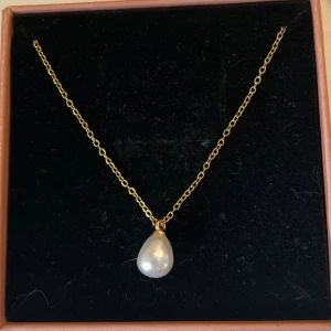 Guldhalsband med pärlhänge - Snyggt halsband med tunn guldfärgad kedja och ett droppformat vitt pärlhänge. Perfekt för dig som gillar klassiska och stilrena smycken med en elegant touch. Passar till alla tillfällen och är lätt att matcha med andra accessoarer. Rostfritt stål och handgjort