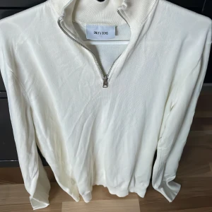 Vit half zip tröja från Only & Sons - Snygg vit långärmad tröja från Only & Sons med ribbad krage och half zip-dragkedja. Tröjan har en clean look och är gjord i mjukt material som känns skönt mot huden. Perfekt för dig som gillar stilrena och enkla plagg.