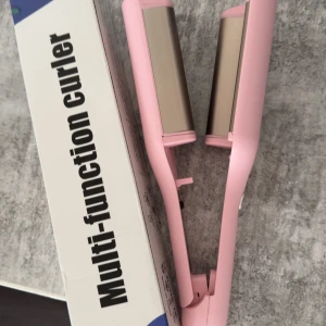 Multi-function Curler - Rosa multi-funktionell locktång med breda plattor, perfekt för att skapa volym och lockar. Produkten ser oanvänd ut och levereras i originalförpackning. Passar för olika hårtyper och stylingbehov.