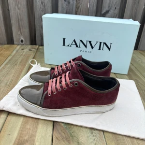 Vinröda sneakers från Lanvin i mocka - Snygga vinröda sneakers från Lanvin med ovandel i mocka och lackad olivgrön tå. Skorna har röd snörning och vit sula med Lanvin-logga undertill. Perfekt för dig som vill ha en unik och lyxig touch på din outfit, nt pris 5000kr mitt pris 1399! Dustbag ingår bara.