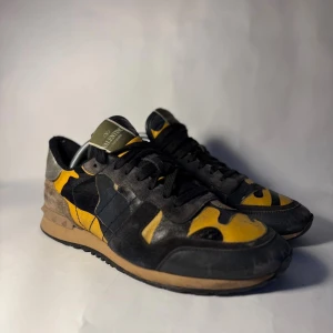 Valentino Rockrunner sneakers camo - Snygga Valentino Rockrunner sneakers med camouflagemönster i svart, gul och beige. Skorna har detaljer i mocka, skinn och textil samt silverfärgad häl. Platt sula med nitar på bakkappan och klassisk snörning framtill. Perfekt för dig som gillar statement-skor.