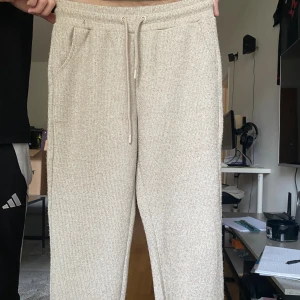 Beige ribbade mjukisbyxor med snörning - Mysiga beige mjukisbyxor med ribbad struktur och snörning i midjan. Perfekta för chill dagar hemma eller när du vill vara bekväm men ändå se fräsch ut. Byxorna har fickor på sidorna och en relaxed fit.