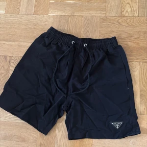 Svarta badbyxor från Prada - Svarta badbyxor från Prada med elastisk midja och snörning. Klassisk design med diskret Prada-logga på vänster ben.  Badbyxorna är i mycket bra skick!! 