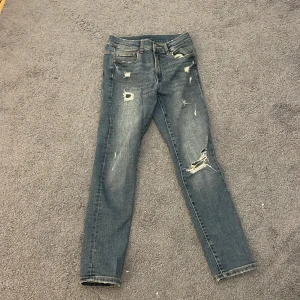 Blå slitna slim jeans från Zara - Säljer ett par blå slim jeans från Zara i storlek 10, med coola slitningar och trasiga detaljer på benen. Jeansen har klassisk femficksdesign och är tillverkade i stretchigt denim för en bekväm passform.