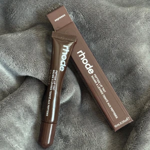 Rhode Peptide Lip Tint Espresso - Helt ny Rhode Peptide Lip Tint i färgen Espresso, en brun tonad läppbalsam i tub. Ger läpparna en snygg brun nyans och återfuktar med peptider. Kommer i en stilren brun förpackning med vitt tryck. Perfekt för dig som vill ha både färg och vård till läpparna.