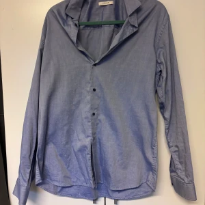 Blå skjorta från Jack & Jones XL - Klassisk blå skjorta från Jack & Jones Premium i storlek XL. Skjortan har lång ärm, knappar framtill och en stilren krage. Tillverkad i mjuk bomull som känns skön mot huden. Perfekt för dig som gillar enkel och clean stil.