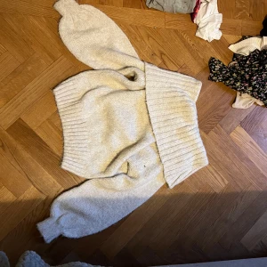 Beige stickad tröja off shoulder  - Mysig beige stickad tröja med bred, ribbad krage och långa ärmar. Tröjan har en relaxed fit och är perfekt för kyliga dagar. Den stickade strukturen ger en skön och trendig känsla.