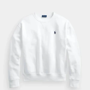 Vit sweatshirt från Polo Ralph Lauren - Vit sweatshirt från Polo Ralph Lauren med klassisk rund hals och broderad marinblå logga på bröstet. Tröjan har långärmad design och ribbade muddar vid ärmslut och nederkant. Perfekt för en clean och stilren look.