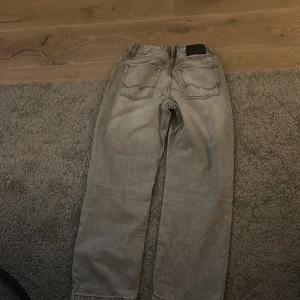 Grå jeans från Jack & Jones - Säljer ett par grå jeans från Jack & Jones med klassisk femficksdesign och raka ben. Jeansen har en snygg tvättad look och normal passform. Perfekta för dig som gillar en enkel och stilren stil. Nästan aldrig använda.