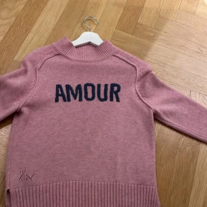 Rosa stickad tröja från Zadig & Voltaire - Lägger upp igen pga oseriösa köpare!Säljer en rosa stickad tröja från Zadig & Voltaire med texten 'AMOUR' i mörkblått på framsidan. Tröjan har långa ärmar och ribbade detaljer vid hals, ärmslut och nederkant. Perfekt för en mysig och stilren look. Pris kan diskuteras vid snabbt köp💞💞