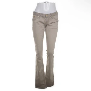 Beiga bootcut byxor med broderi - Snygga beiga bootcut-byxor med guldigt broderi av vingar på bakfickorna. Byxorna har klassisk femficksdesign, låg midja och stängs med knapp och dragkedja. Perfekta för dig som vill ha en cool och unik detalj på dina byxor.storlek w31 skulle säga en Medium!