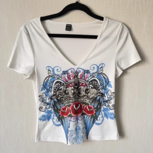 Vit croppad topp med krona och rosor - Säljer en vit croppad topp med v-ringning.