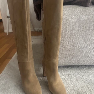 Beiga mockastövlar med klack - Snygga höga stövlar i äkta mocka från NA-KD i beige mocka med spetsig tå och stabil klack. Dragkedja på insidan för enkel påtagning. Storlek 37, aldrig använda.  Länk: https://www.na-kd.com/sv/produkter/suede-knee-high-boots-dusty-beige-1055-001438-9673?_kx=JBP0myrGE9U1lcM5B70XVCSUKz-OLKbMGWPLr6a81BzItUAVWfmSpHsnzVaER3tT.PF6Tdw