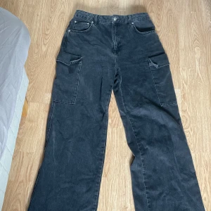 Svarta cargopants med raka ben - Säljer ett par svarta cargopants med raka ben och stora fickor på sidorna. Byxorna har klassisk femficksdesign framtill och fickor med lock bak. Perfekta för dig som gillar en avslappnad och trendig stil.
