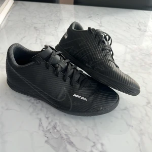 Nike Mercurial svarta fotbollsskor inomhus - Svarta Nike Mercurial inomhusfotbollsskor . Skorna har snörning och en ribbad syntetisk yta för extra grepp. Perfekt för dig som vill ha stilrena och snabba skor på planen. Priset går att diskutera!